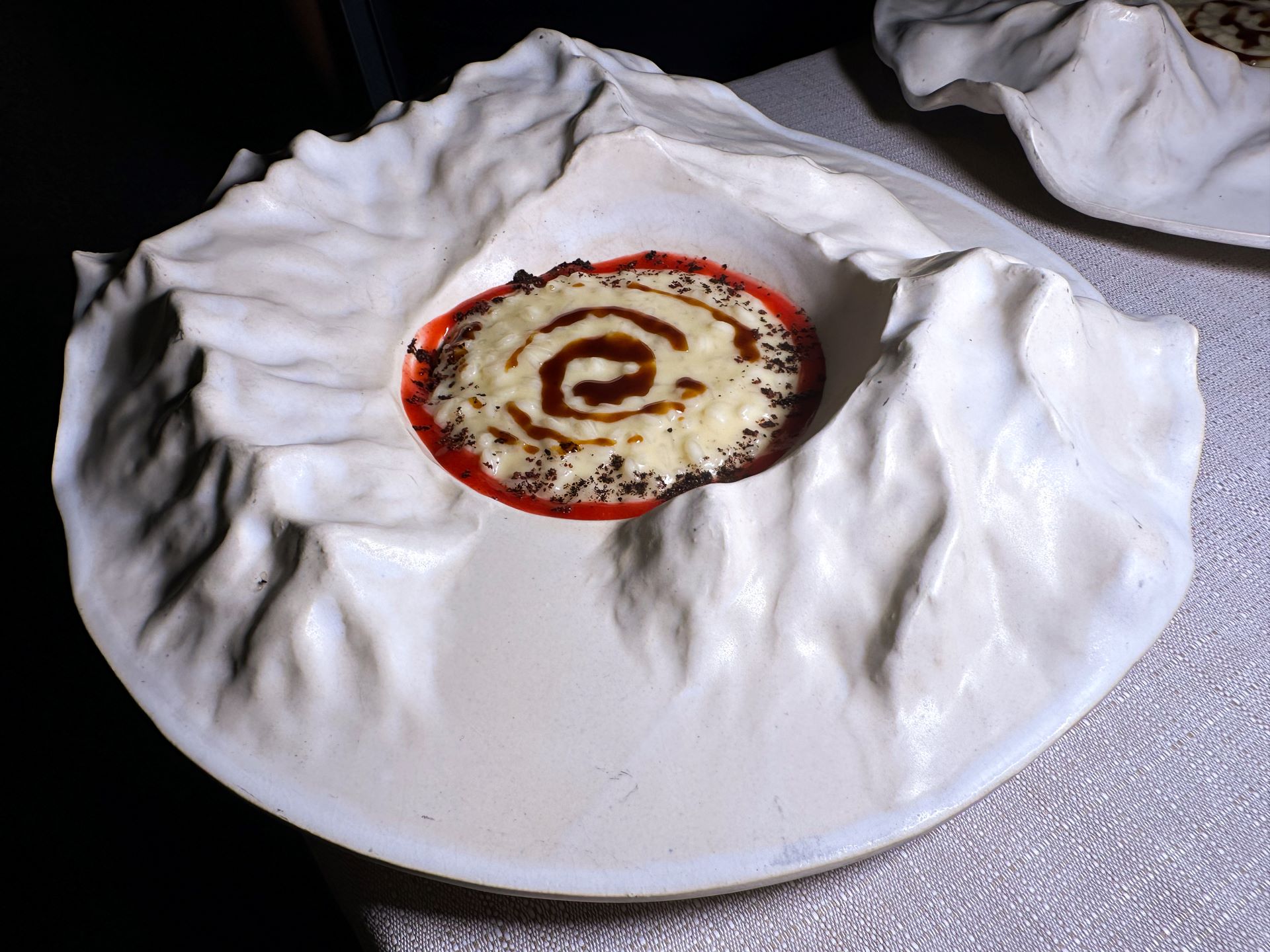 Iconico risotto dell'agriturismo Ferdy: Riso Carnaroli al latte, salsa romice, fondo bruno, fave di cacao e polvere di abete.