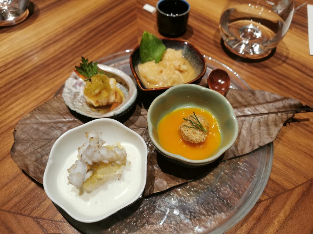 Hassun – Composizione di antipasti: merluzzo al miso, Gambero al porro e yuzu, Capasanta con purea di zucca, patata affumicata al tè, calamaro e brie.