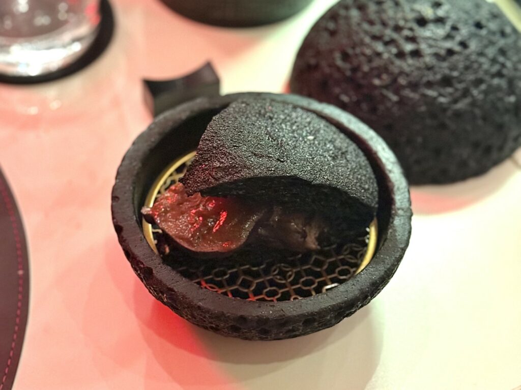 Bao impastato al carbone vegetale cotto al vapore, guancia di maiale brasata e la sua demiglace della pizzeria quattro quarti.