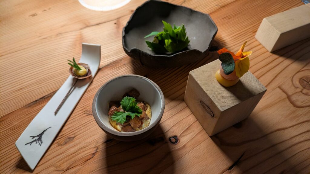 Miniature Wild: crema fredda di geranio fegato di cervo al gin e rosa selvatica; cuore di cervo marinato e torba di pino mugo; streusel di calendula, nasturzio e coregone affumicato; levistico, robiola di montagna e cenere di pigna fermentata.