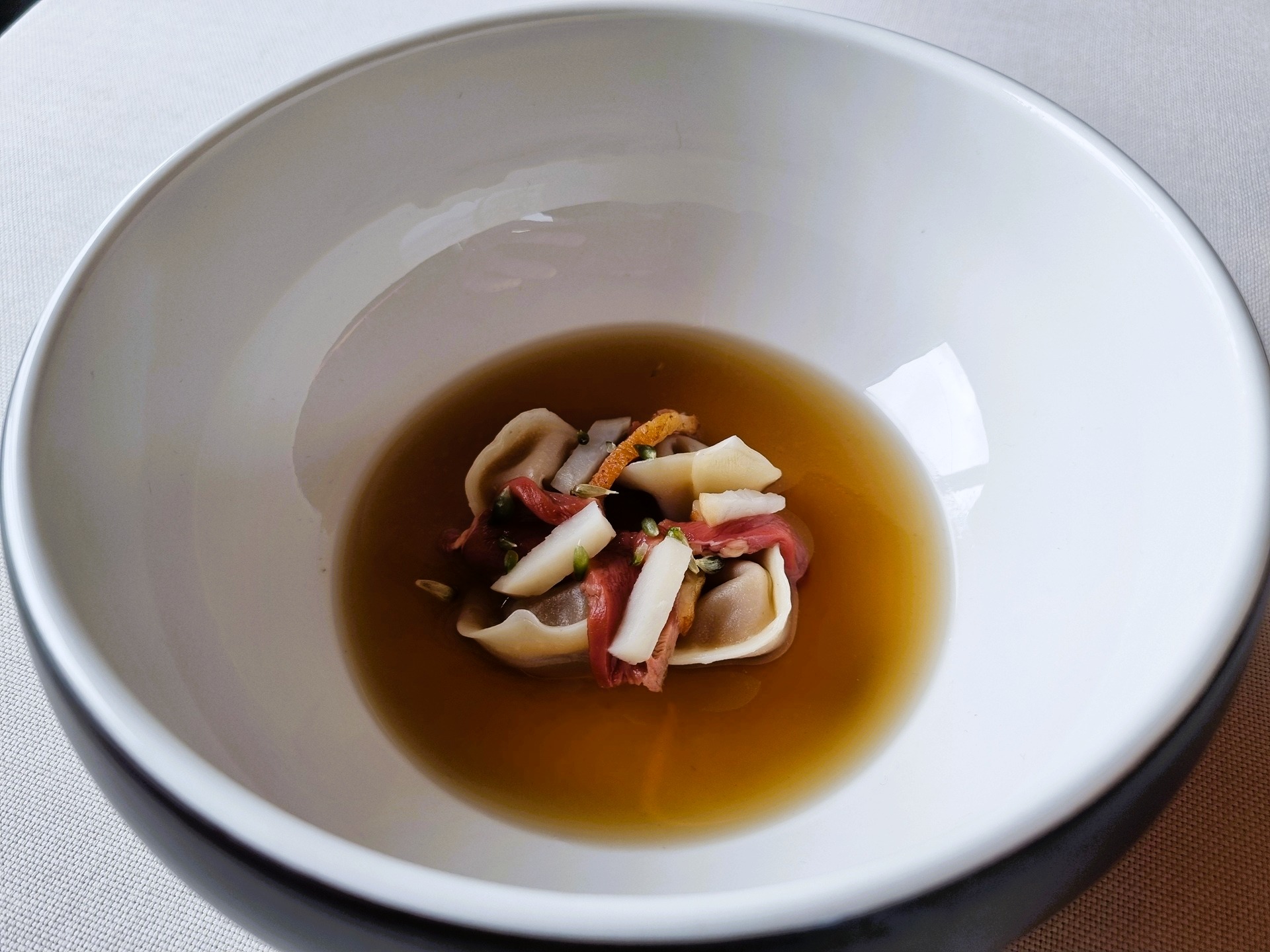 Ravioli di pasta di mandorle con ripieno di albicocca, brodo di ossa e interiora di piccione, semi di aglio selvatico, topinambur del ristorante la tana gourmet