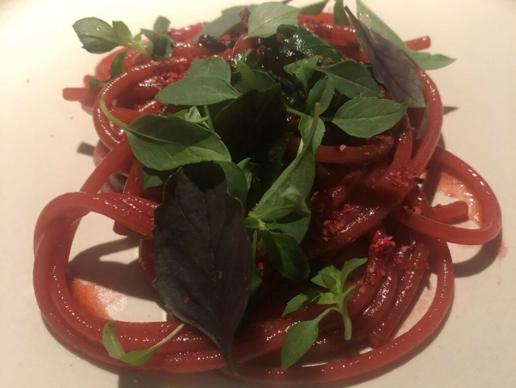 Spaghetto al pomodoro senza pomodoro, (estrazione di fragole), pepe rosa, basilico greco e basilico viola.