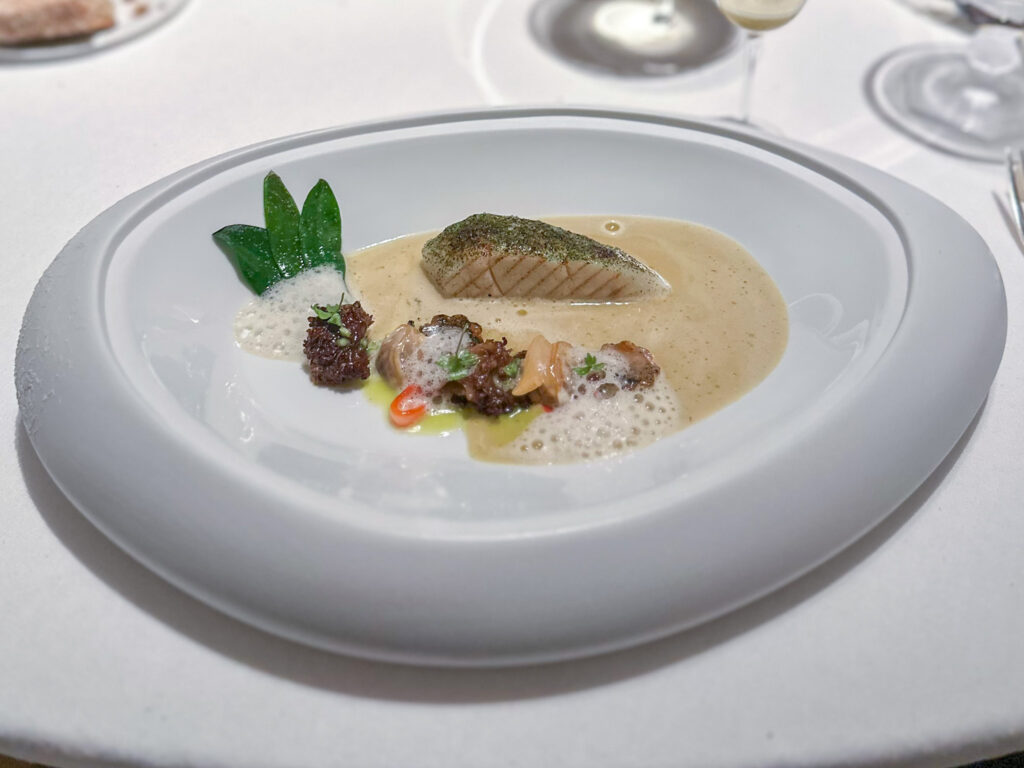 Branzino / Spugnola di pino / Levistico & Bouillon “Iodé Boisé”, salsa fatta da succo di abalone, essenza di spugnola, burro nocciola, sedano selvatico, olio d’oliva infuso al levistico, vermouth, porcino disidratato, bacca di macerone.