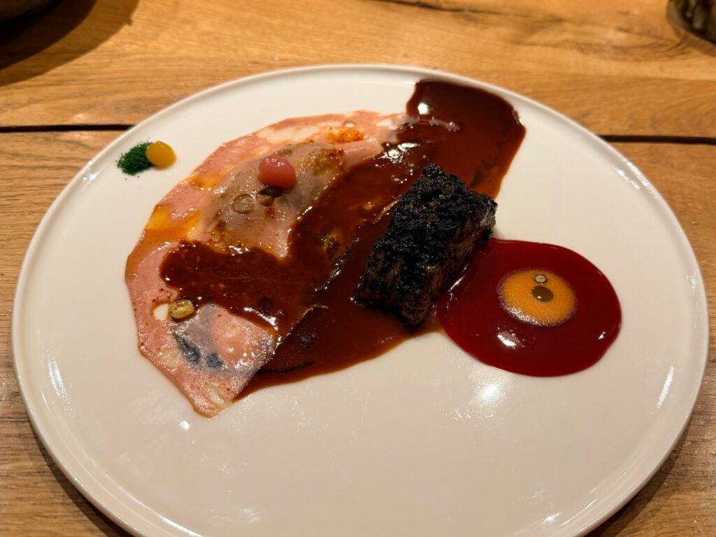 Nasello pescato con la lenza, scottato come un satay, gel agrodolce, mortadella, fondo d’anatra al pepe e verbena